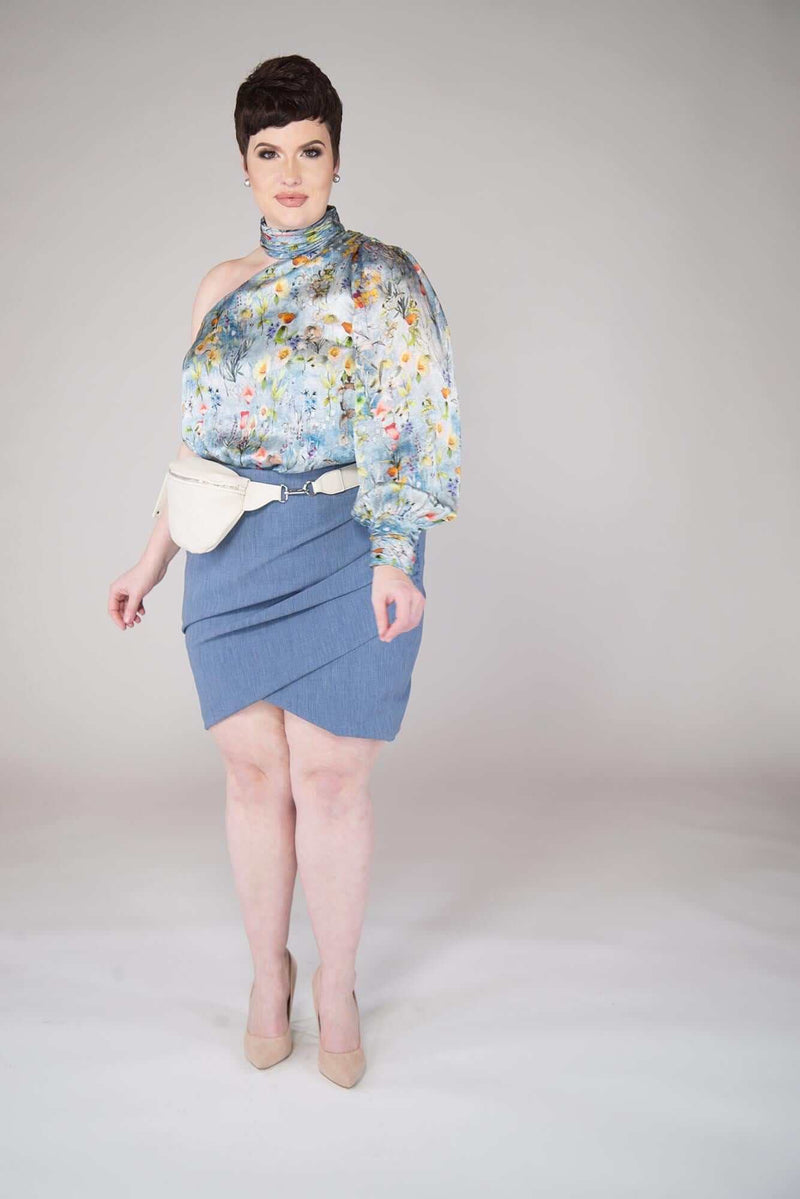 short haired model wears a Campanula Blue colored Tulip Mini Skirt with End on End Texture with a True Waisted with Side Ruching and Crossed Front Hem Details include: Full Garment Lining and Center Back Invisible Back Zipper. Fabric is Viscose/Poly/Spandex  garment is MADE IN NEW YORK CITY BY Mayes NYC